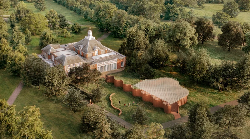 Aerial view of a large historic brick building next to a modern, curved pavilion surrounded by green trees and grassy landscape.