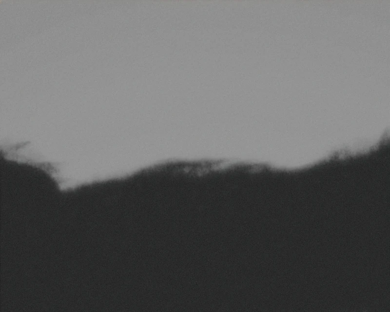 A silhouette of a hilly landscape against a gray sky.