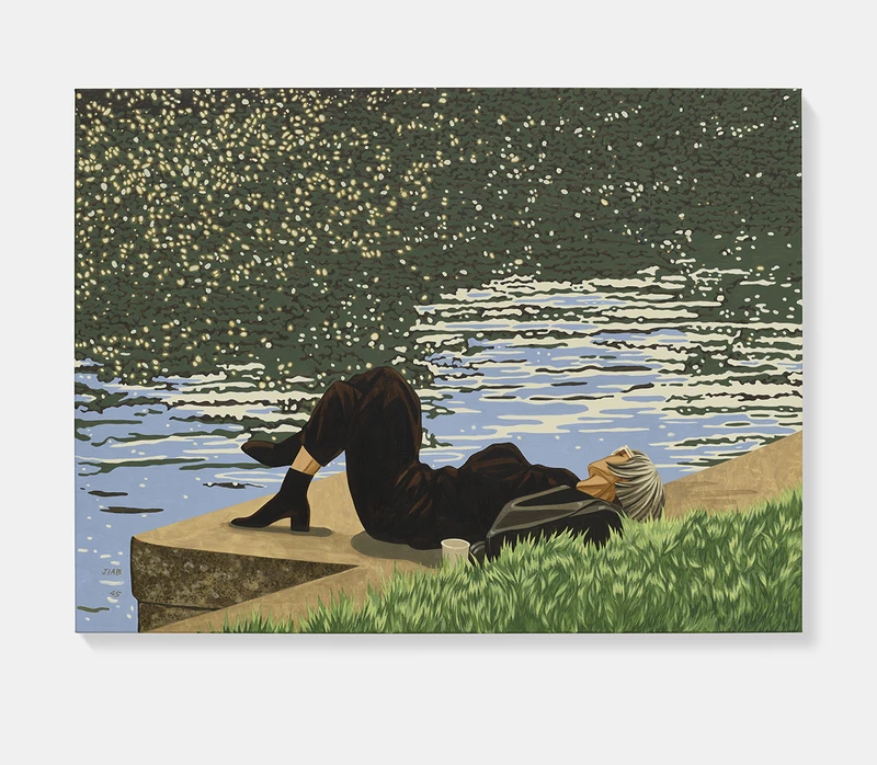 A person reclining by a shimmering body of water, surrounded by grass, wearing dark clothing and sunglasses.
