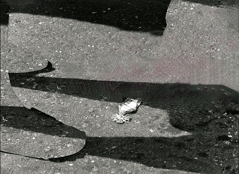 A close-up of a street showing a small object on the pavement, surrounded by shadowed figures.
