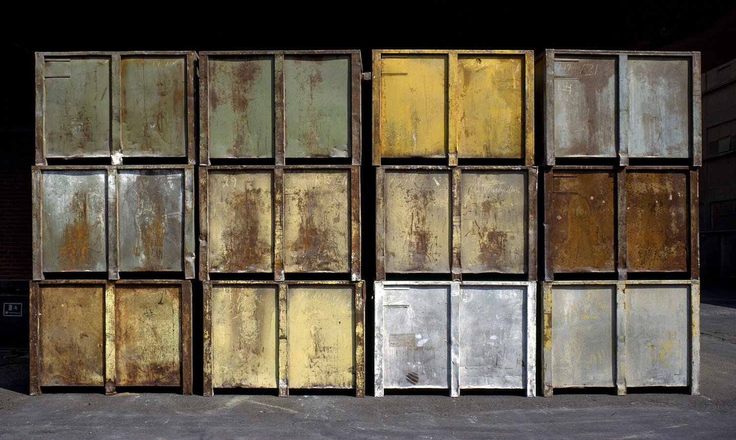 A series of weathered and rusted metal containers in various colors, including green, yellow, and silver, arranged in a grid pattern.