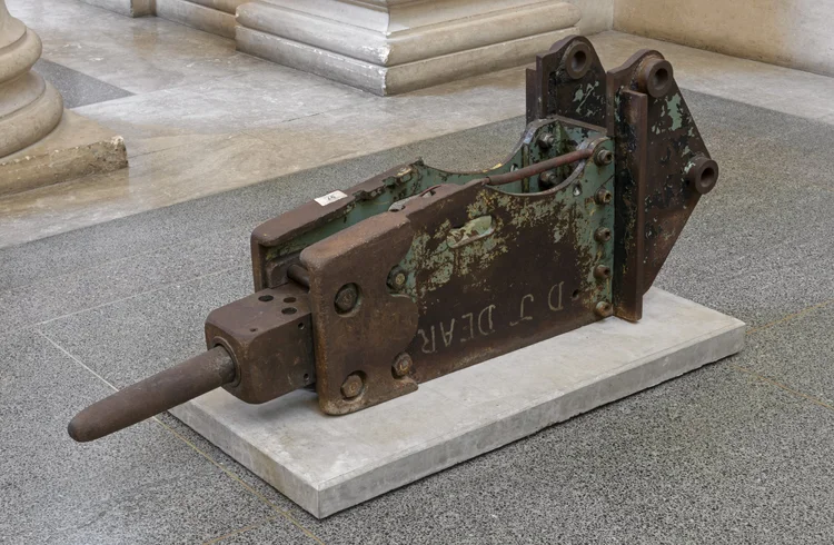 An empty art gallery with several colorful paintings on the white walls, featuring a gray floor and large windows.