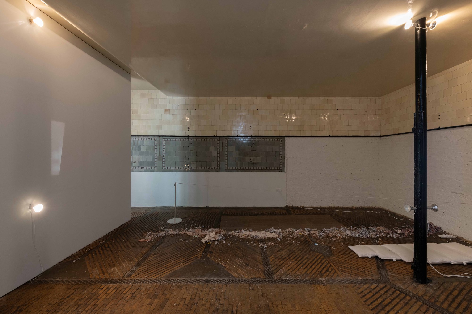 An empty room with peeling walls, some debris on the floor, and a single light fixture.