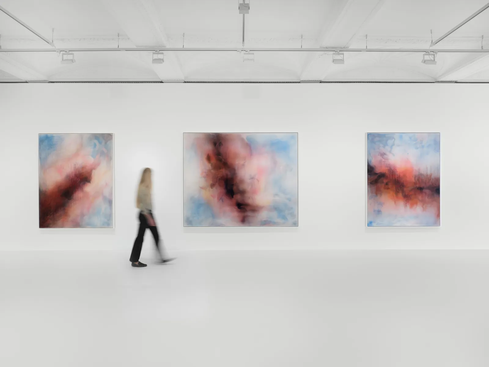 A person walking past abstract paintings in a gallery.