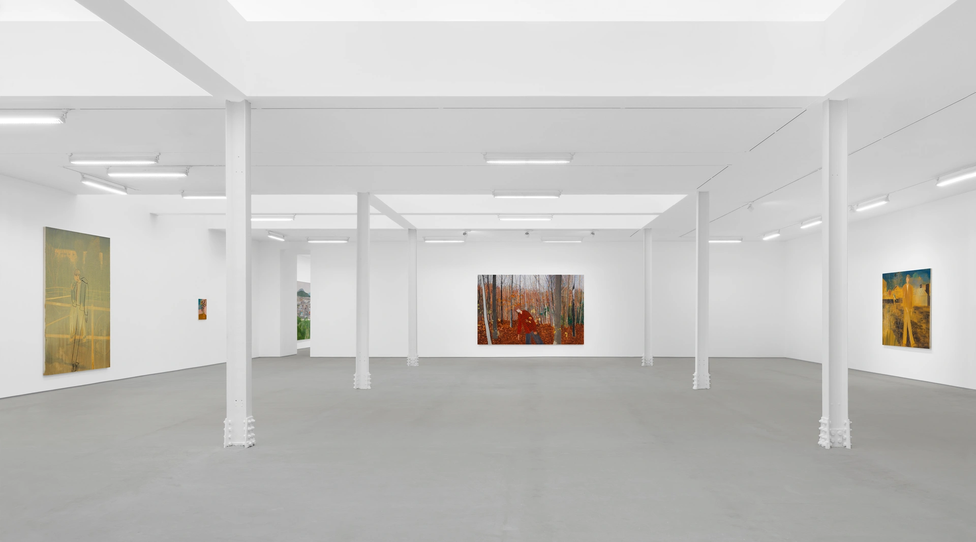 An empty art gallery with white walls and gray floors, displaying several paintings.