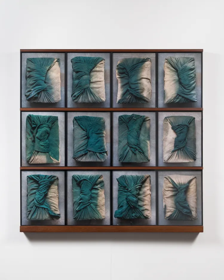 A grid of twelve textured artworks, each featuring wrinkled and draped fabric in deep teal against a neutral background, arranged in a rectangular frame.