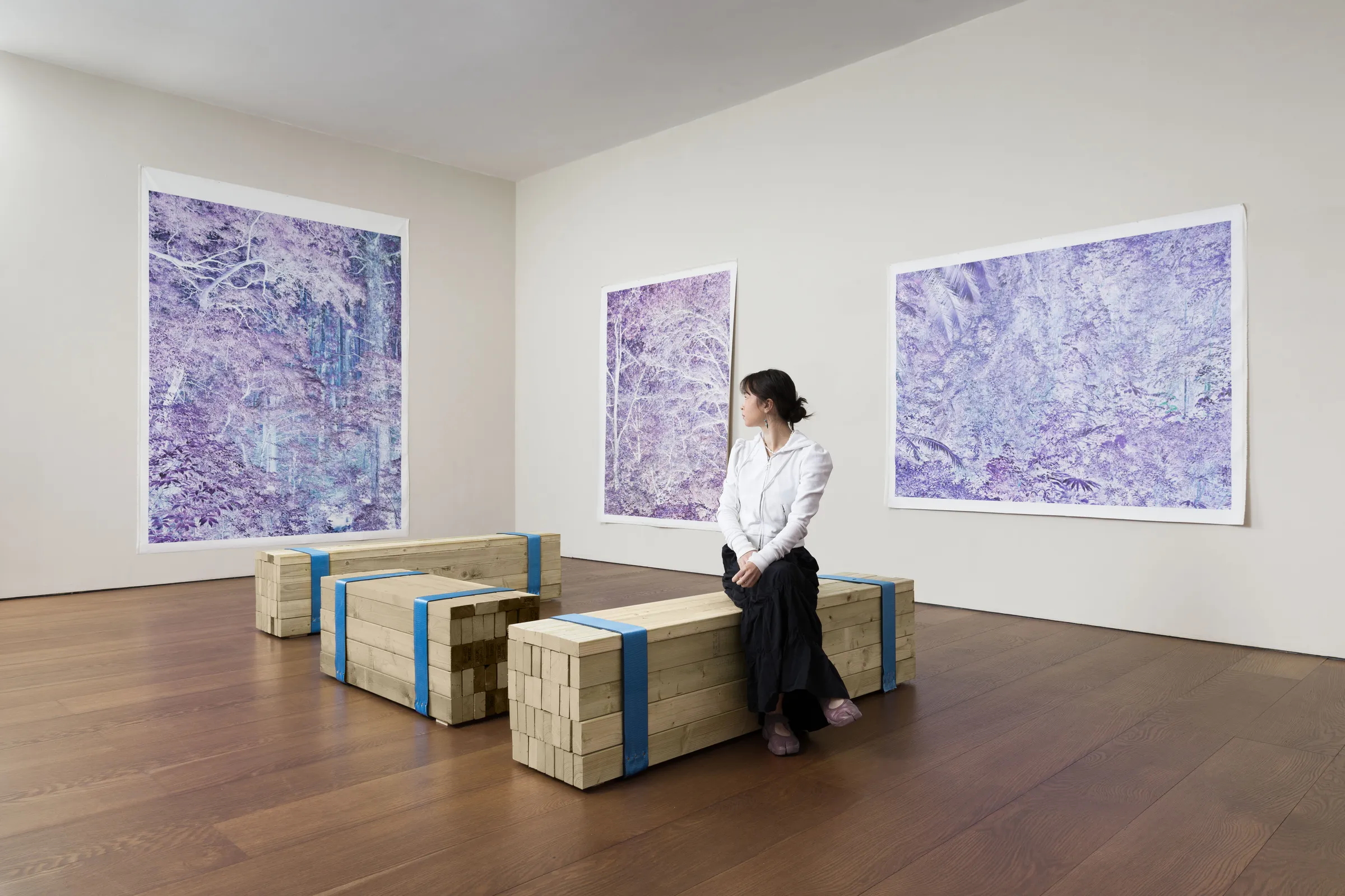 A woman sitting on a wooden bench in an art gallery, surrounded by large purple abstract paintings on the walls.