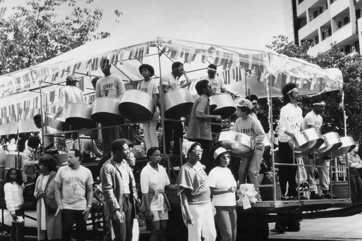 A group of people playing steel drums on a float at a parade, surrounded by spectators.