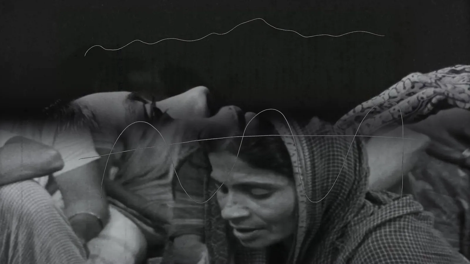A black and white image of a woman wearing a scarf, engaged in conversation with others in a blurred background.
