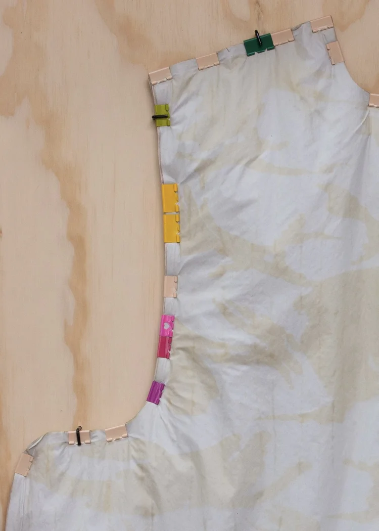 A piece of fabric pinned with colorful clips on a wooden surface.