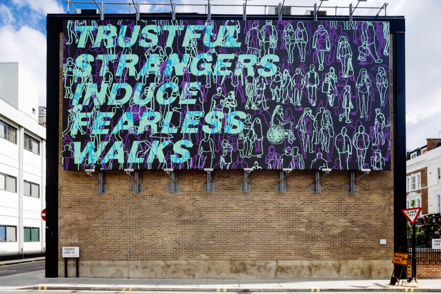 A large mural on a building featuring words Trustful Strangers Induce Fearless Walks with a background of outlined figures.