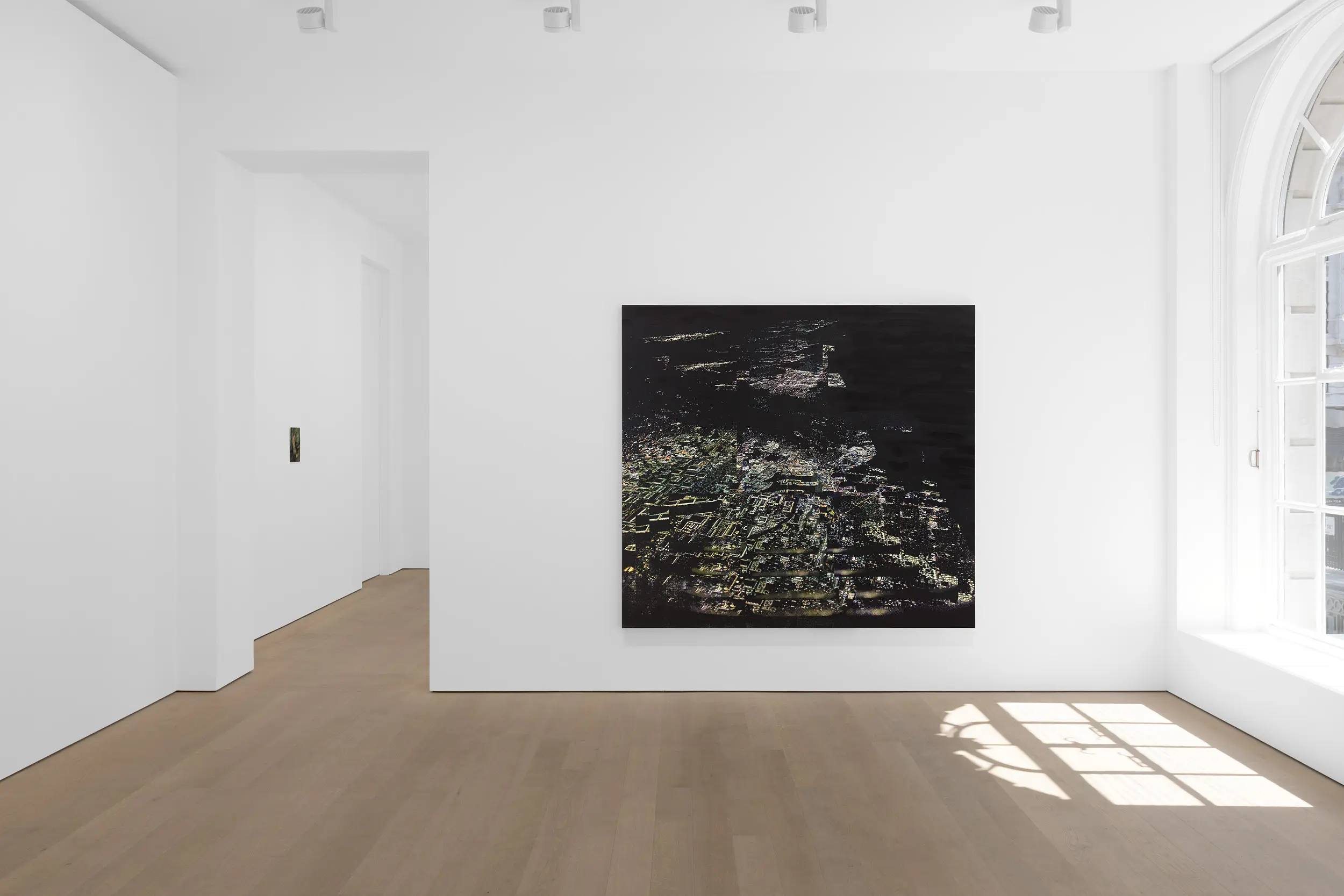 A minimalist art gallery with a large dark painting on the wall and light-colored wooden flooring.