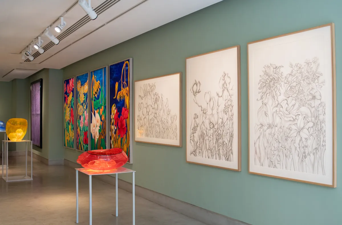 A modern art gallery showcasing colorful floral paintings and sketches on display, with a translucent sculpture in the foreground.