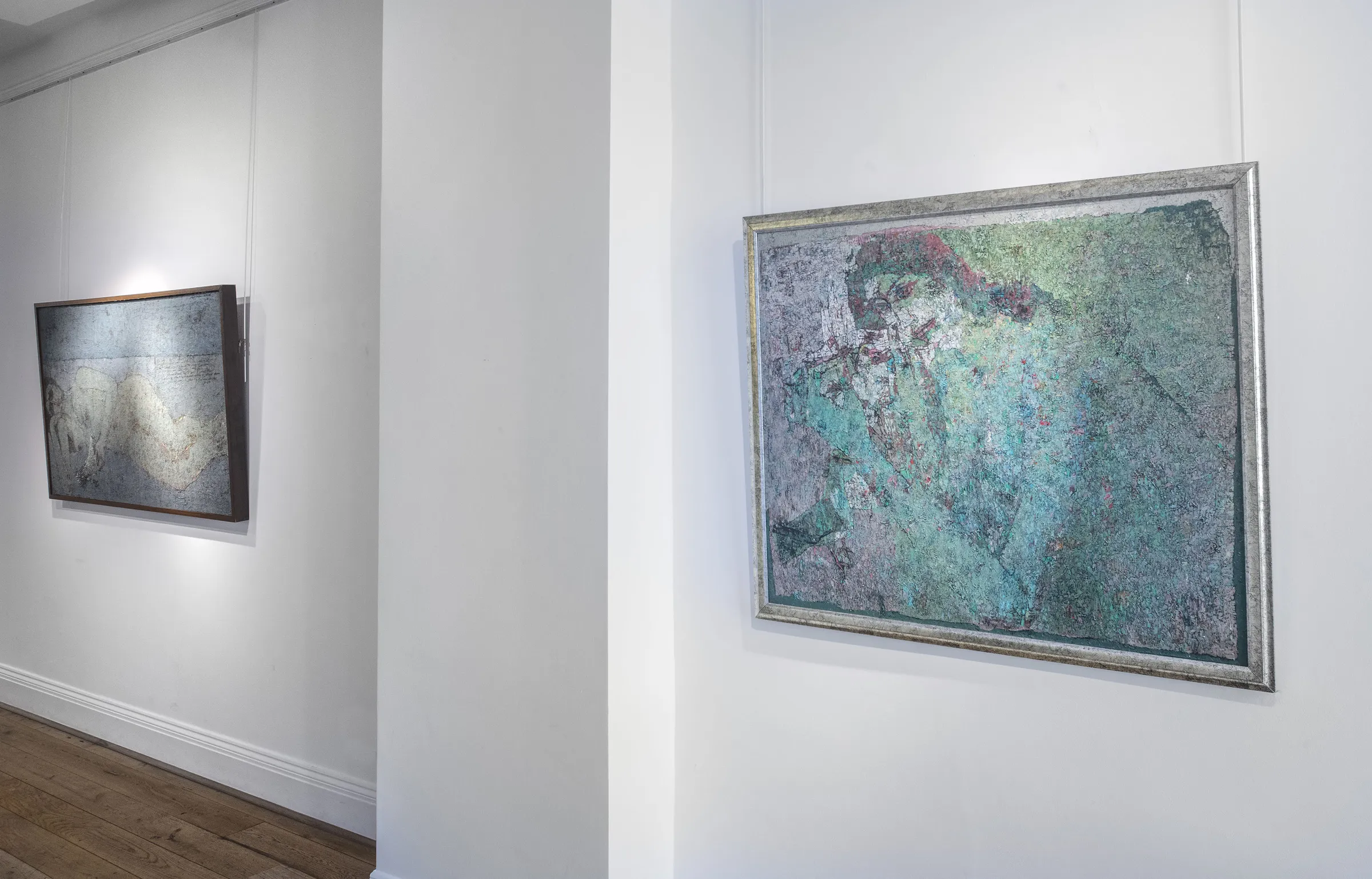 Two abstract paintings on display in a gallery, with one framed piece hanging on a white wall.
