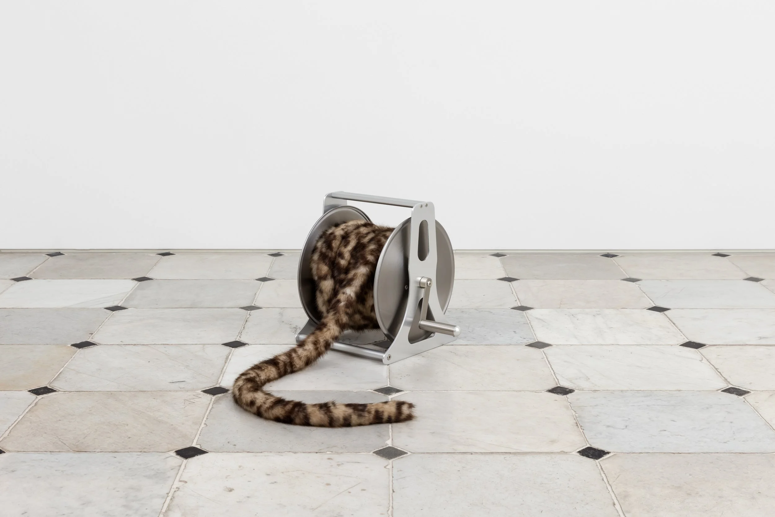 A metal reel with a faux fur tail spilling out, placed on a tiled floor.