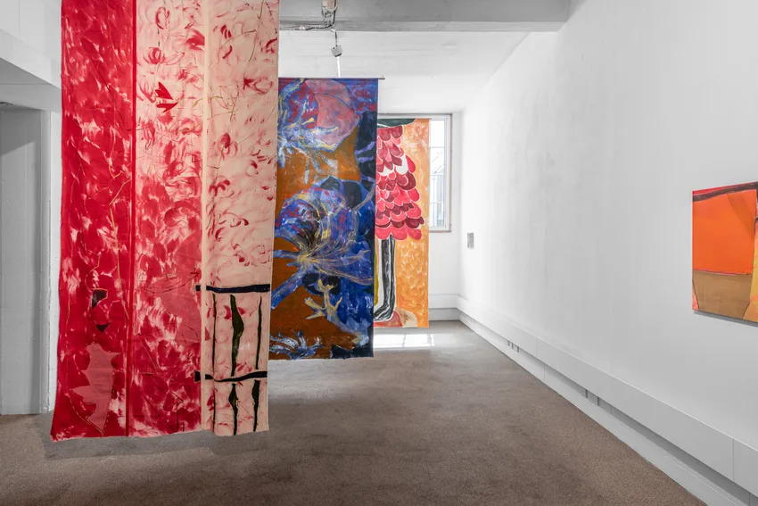 An interior space with colorful fabric panels hanging from the ceiling, featuring red, blue, and orange hues, along with a small artwork on the wall.