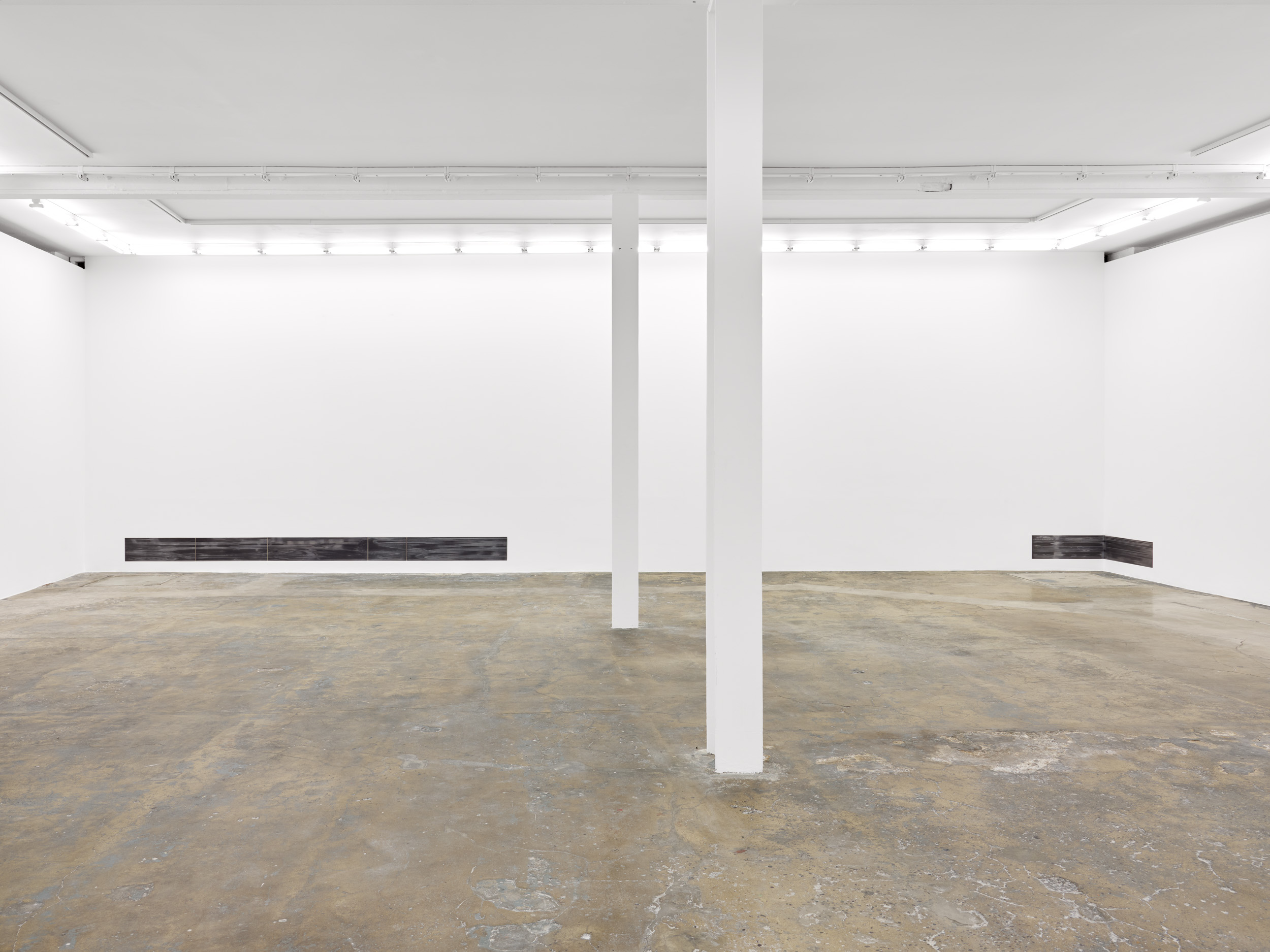 Minimalist white art gallery with two central columns, bare concrete floor, and low dark artworks along back walls; quiet, stark mood.