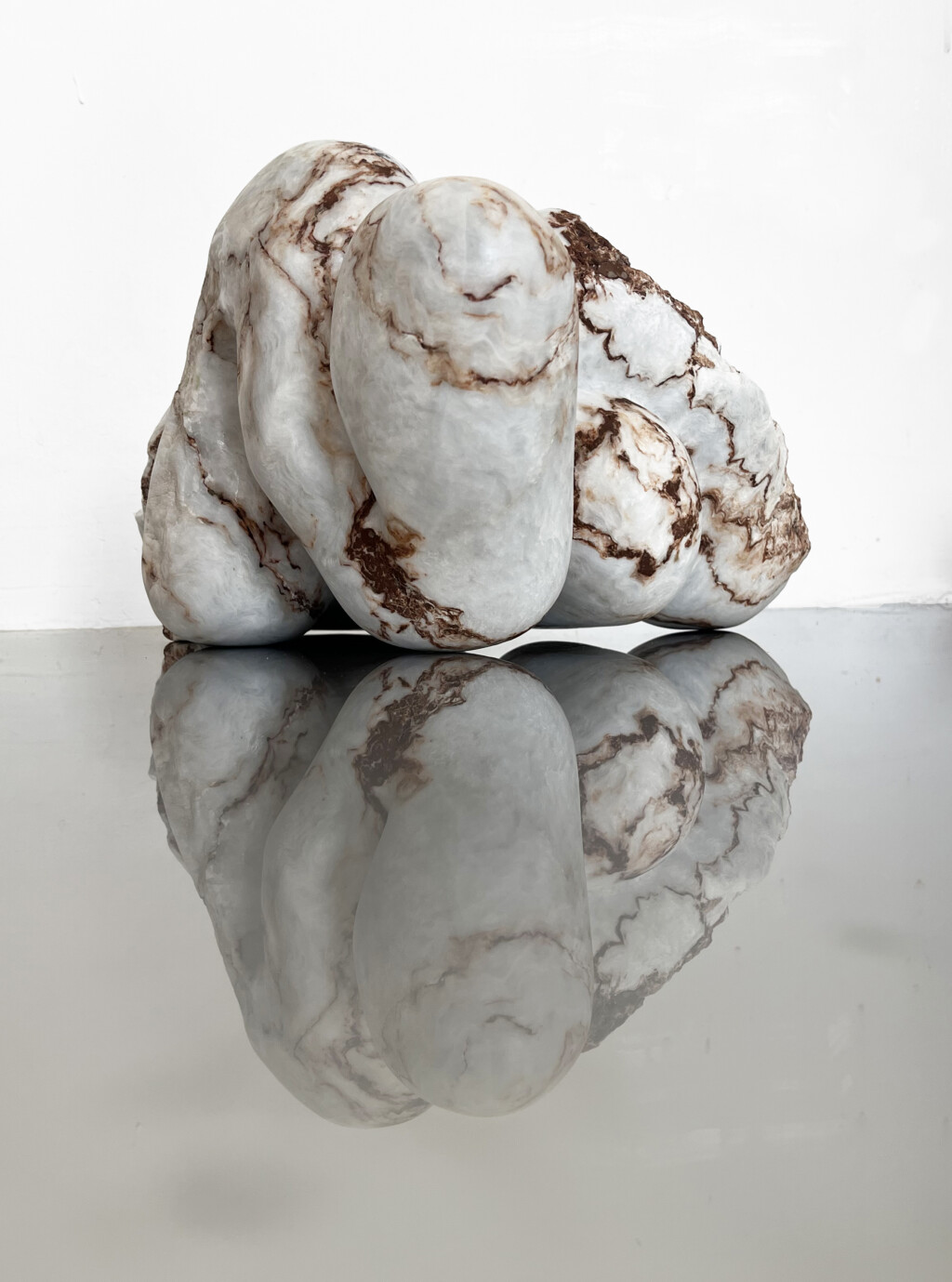 Three large, smooth white stones with brown marbled veining are stacked on a glossy surface, their reflections creating a calm, sculptural still life.