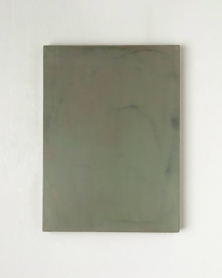 A plain, muted olive-gray rectangular canvas or panel hangs against a white wall, its smooth surface subtly marked by faint shadows and stains, creating a quiet, minimalist mood. | 2026 Bartha Contemporary