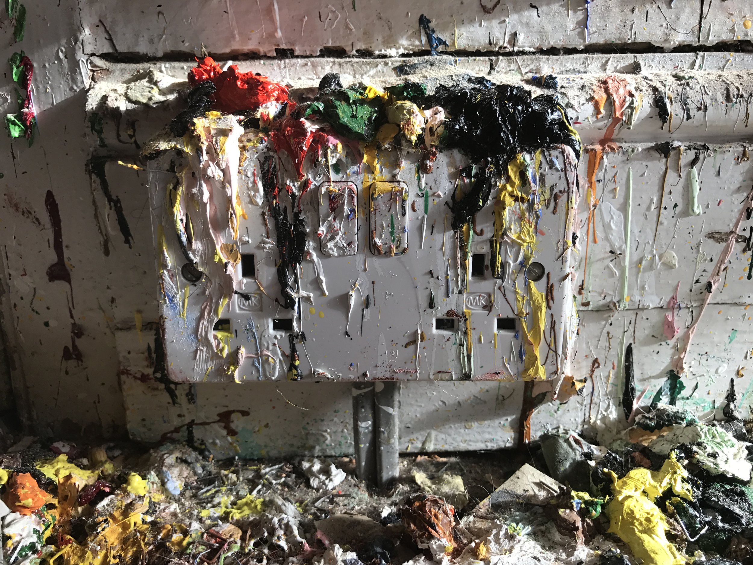A paint-encrusted studio wall and worktable, streaked with dripping red, green, yellow, and black paint; scattered scraps create a raw, energetic mood. | 2026 A.P.T. Gallery