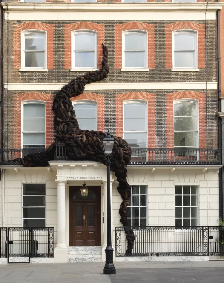 A life-size black chain sculpture snakes up the red-brick façade of a London townhouse, draping over windows and a balcony for a striking, surreal effect. | 2026 Annely Juda Fine Art